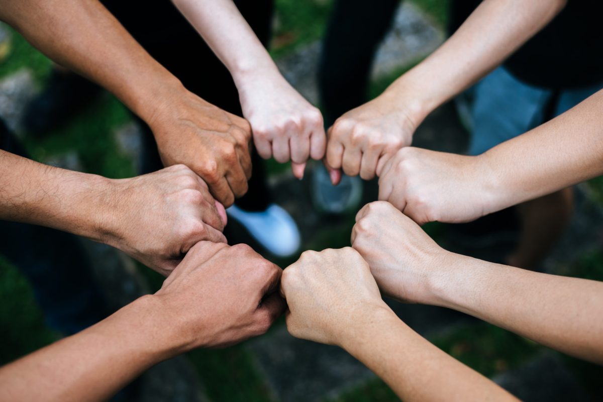 Close up of students standing hands making fist bump gesture.