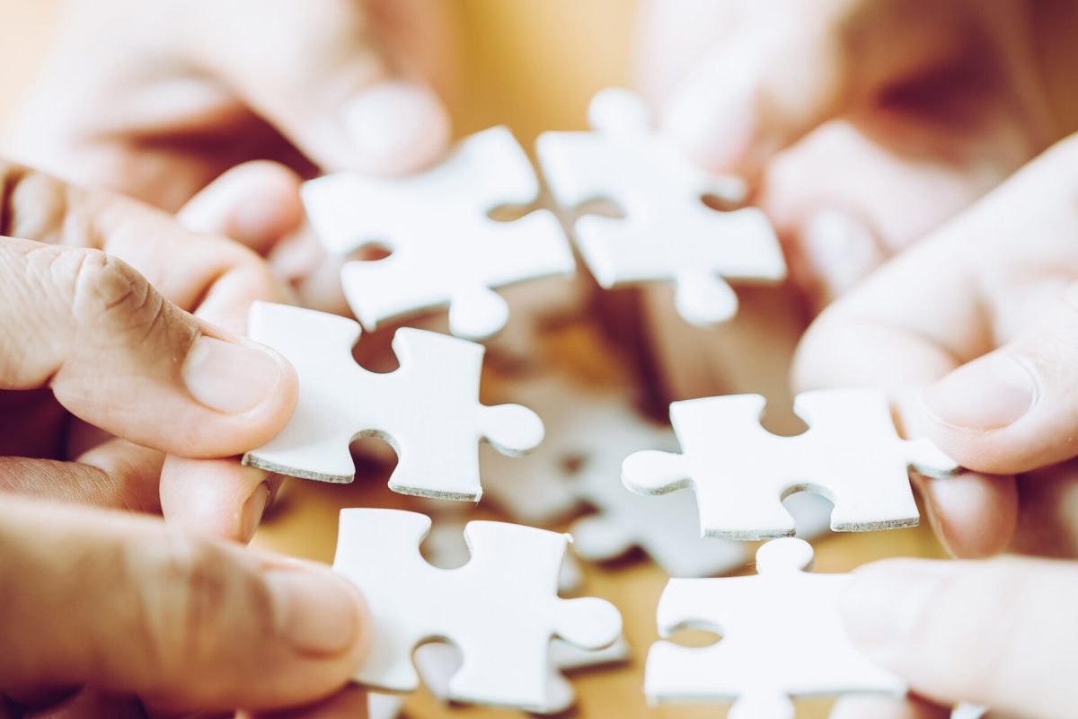 Hands of a person little child and parent playing jigsaw puzzle piece game together on wooden table at home, concept for leisure with family, play with children's development, education and fun.